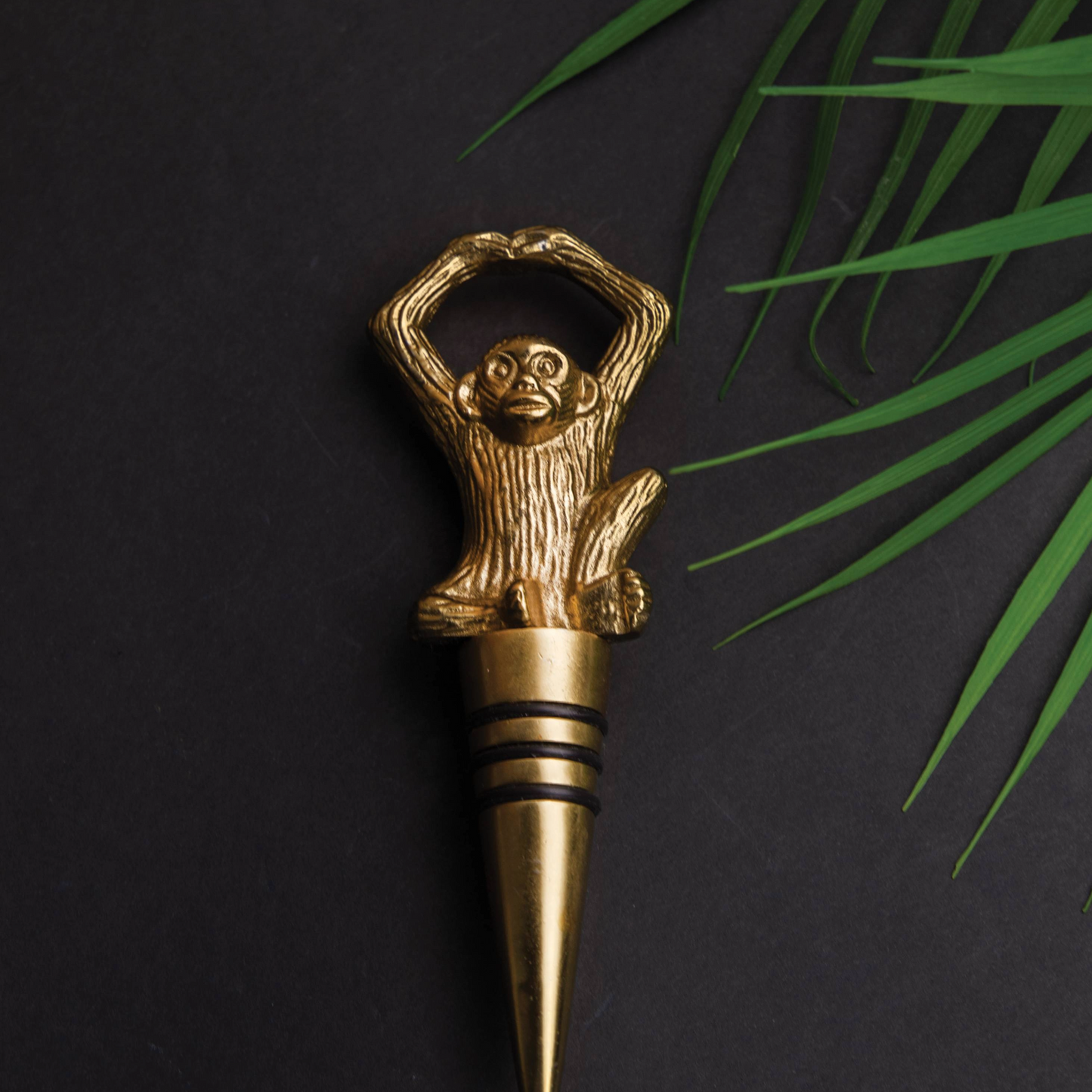 Gouden flessenstop met aapmotief op donkere achtergrond en palmtakken – elegant en speels design, verkrijgbaar bij Sherlocks Place. Voor stijlvolle wijnliefhebbers en interieurdecoratiefans.
