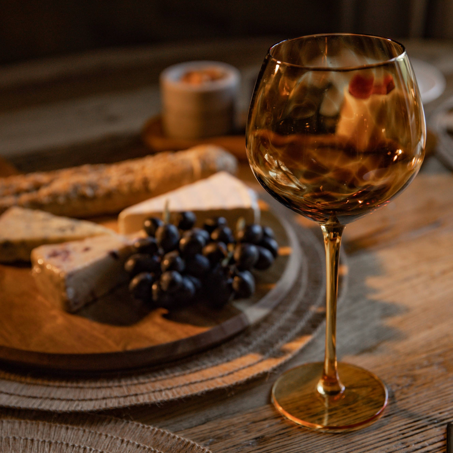 Avondsfeer met een gevuld gin glas naast een kaasplank met druiven en stokbrood, op een rustieke houten tafel. Verkrijgbaar bij Sherlocks Place