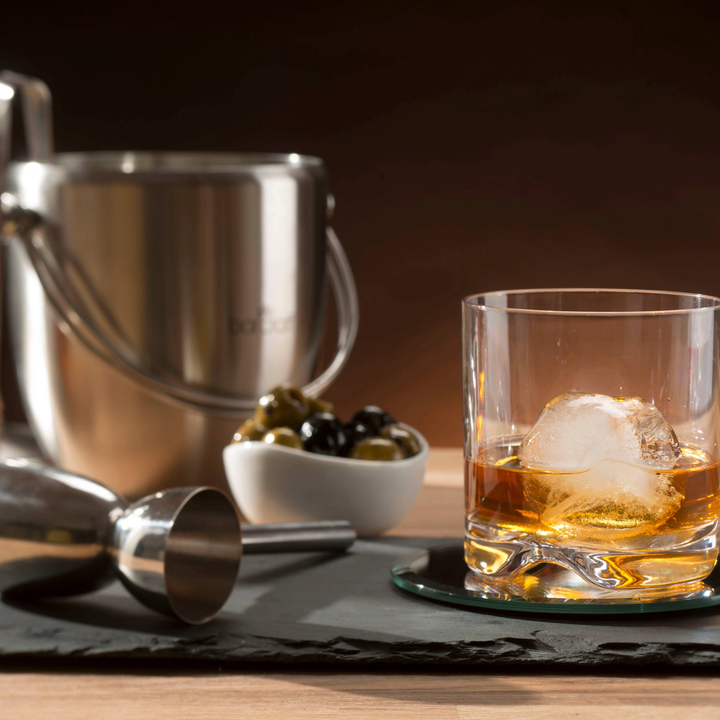 (sfeershot met glas en cocktailaccessoires)
Sfeervolle setting met BarCraft ijsemmer, whiskyglas en cocktailtools – de ultieme sfeer voor een avond borrelen. Verkrijgbaar bij Sherlocks Place.