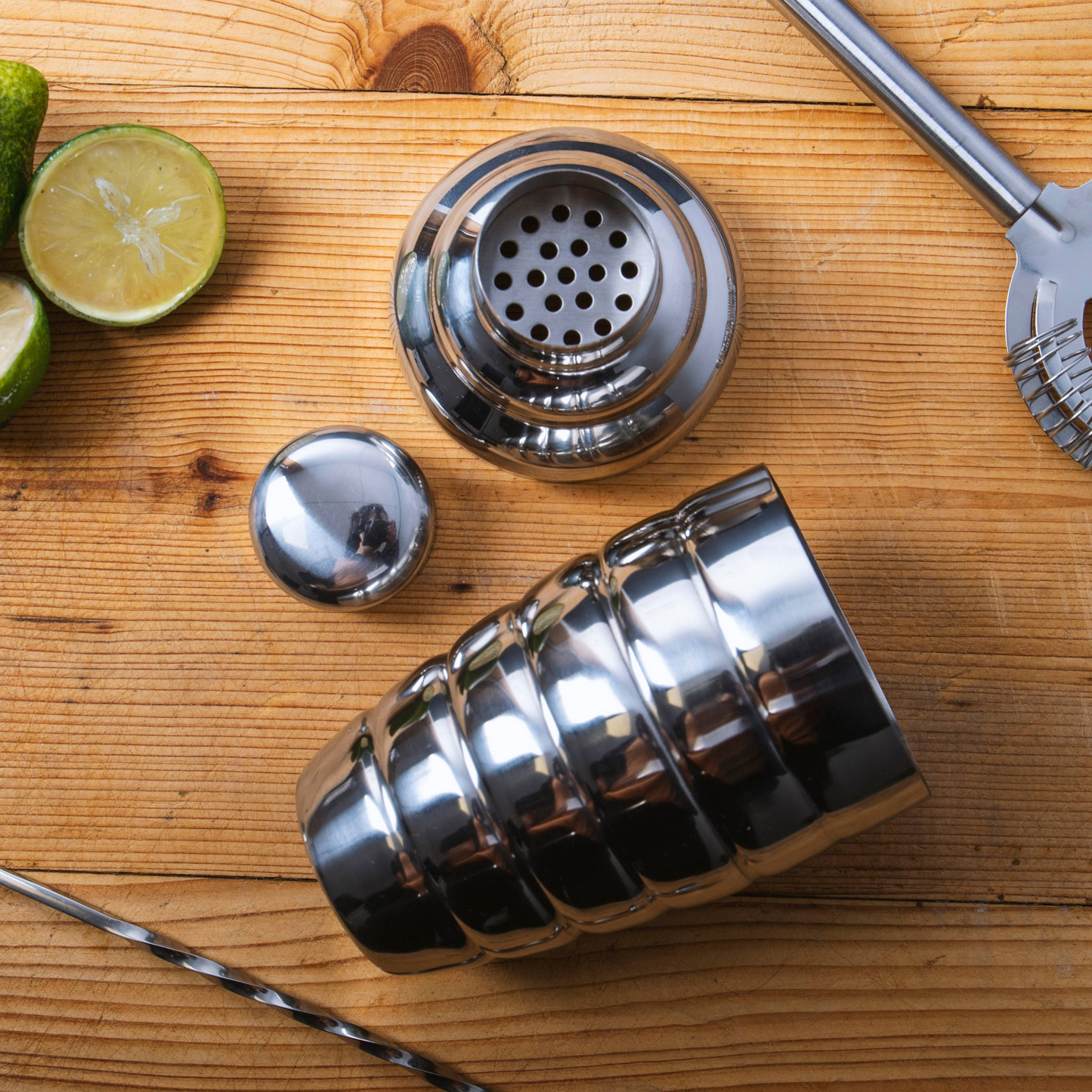 Roestvrijstalen cocktailshaker in gebruik met cocktailaccessoires en limoenen – Verkrijgbaar bij Sherlocks Place