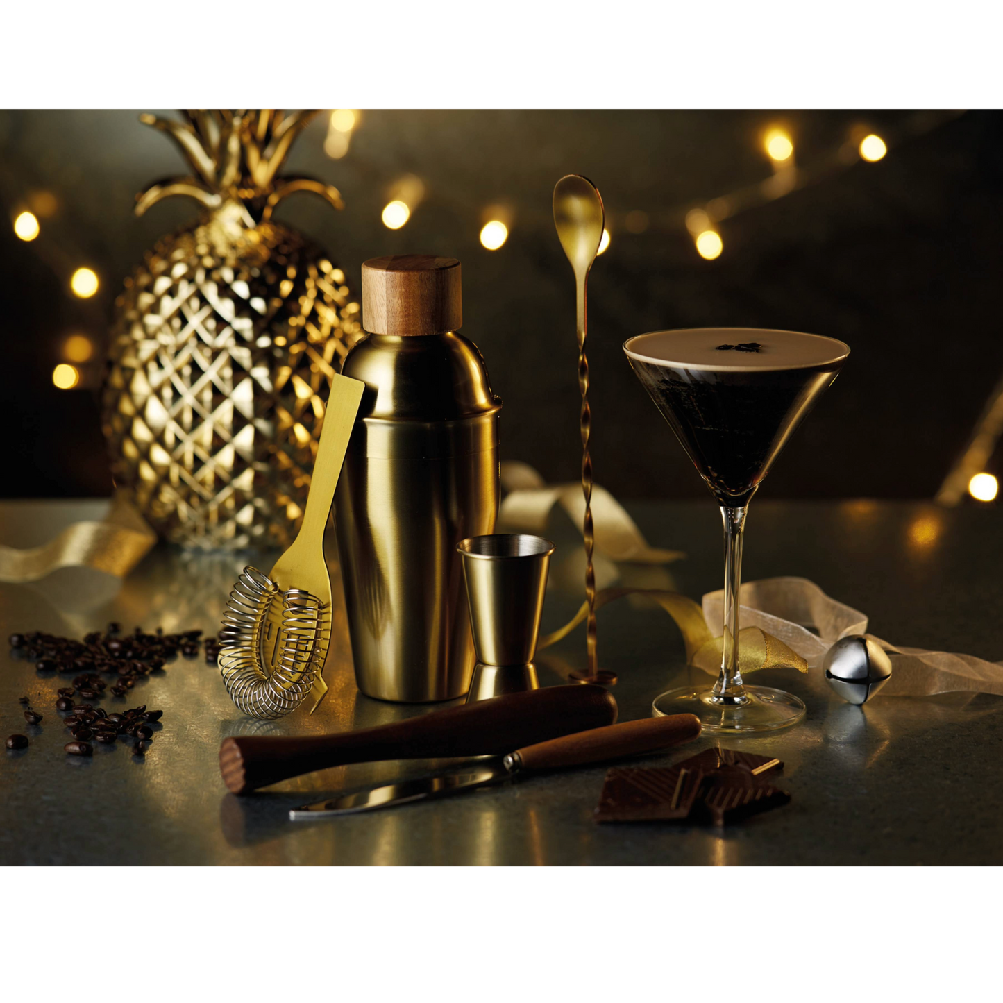 Sfeervolle setting met gouden cocktailset, espresso martini en feestverlichting – perfect voor de feestdagen of als uniek cadeau – verkrijgbaar bij Sherlocks Place.