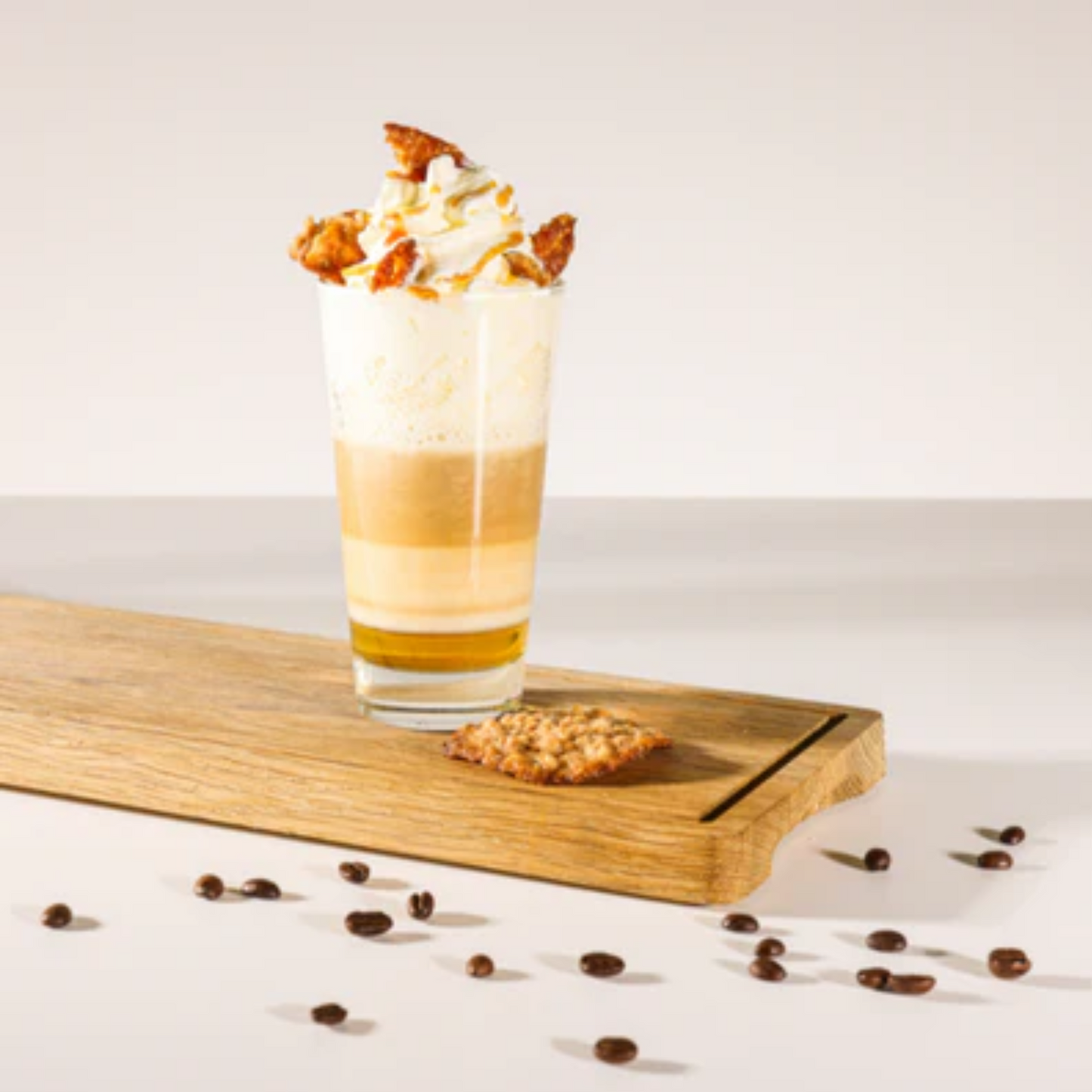 Crem Brûlee en Nougat Latte met Monin. Afgewerkt met een toef slagroom en stukjes kletskop-koekjes. Op een houten serveerplank, omringd met koffieboontjes. Het glas laat mooi de lagen van een latte zien: siroop, melk, koffie, melk en topping. Perfect voor zoete latte liefhebbers. Compleet Monin assortiment verkrijgbaar bij Sherlocks Place Rotterdam
