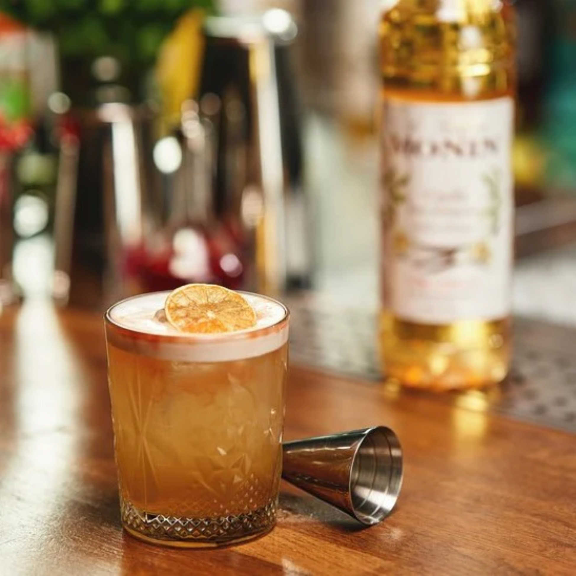 Verfrissende Bourbon Sour met MONIN Vanille en Mandarijn siroop, geserveerd in een kristallen glas – fles verkrijgbaar bij Sherlocks Place Rotterdam.