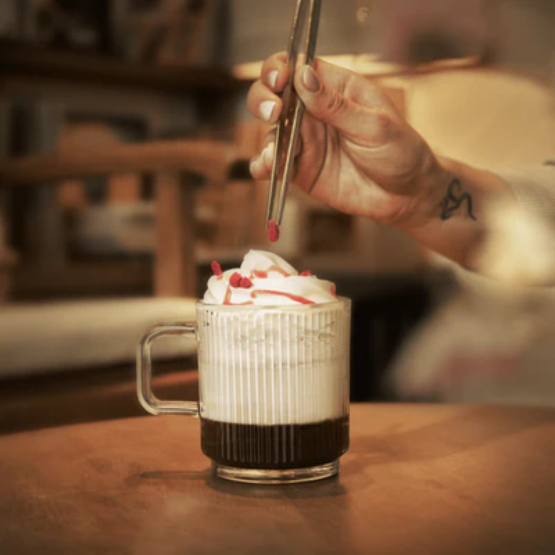 Een luxe Brazilian Hot Chocolate verrijkt met MONIN Macaron siroop, afgewerkt met slagroom en rode topping, geserveerd in een glazen mok. Monin verkrijgbaar bij Sherlocks Place in Rotterdam