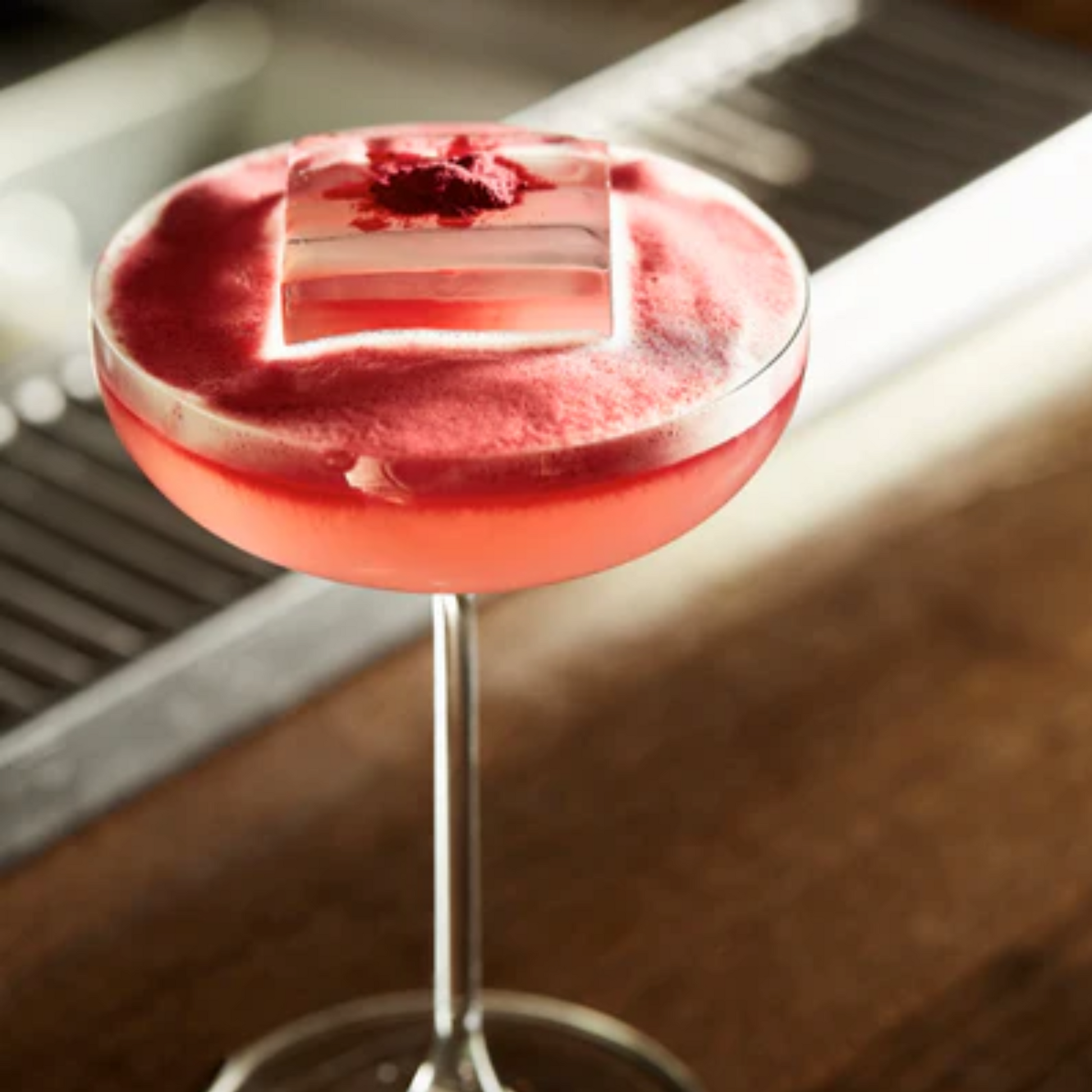 Minimalistische close-up van een Strawberry Daiquiri in een martini glas met mooie schuimkraag en afgetopt met een roze vierkant ijsblokje in het midden van het glas. Monin Strawberry perfect voor cocktails, lemonades en ijscreaties. Verkrijgbaar bij Sherlocks Place Rotterdam