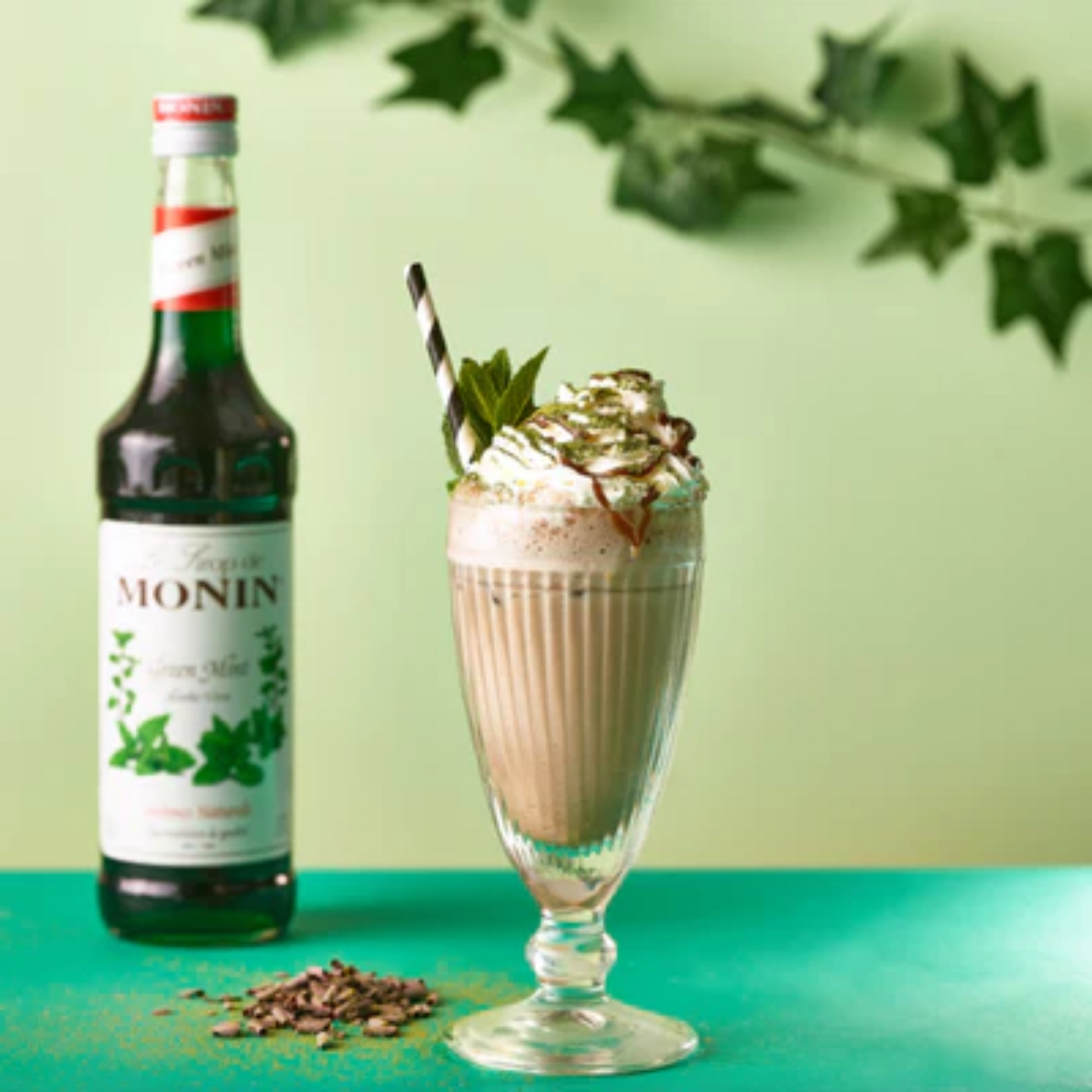 Frozen banaan-munt milkshake geserveerd met slagroom, chocoladesaus en verse munt, naast een fles Monin Green Mint siroop – zomerse traktatie met tropische twist. Monin verkrijgbaar bij Sherlocks Place Rotterdam 