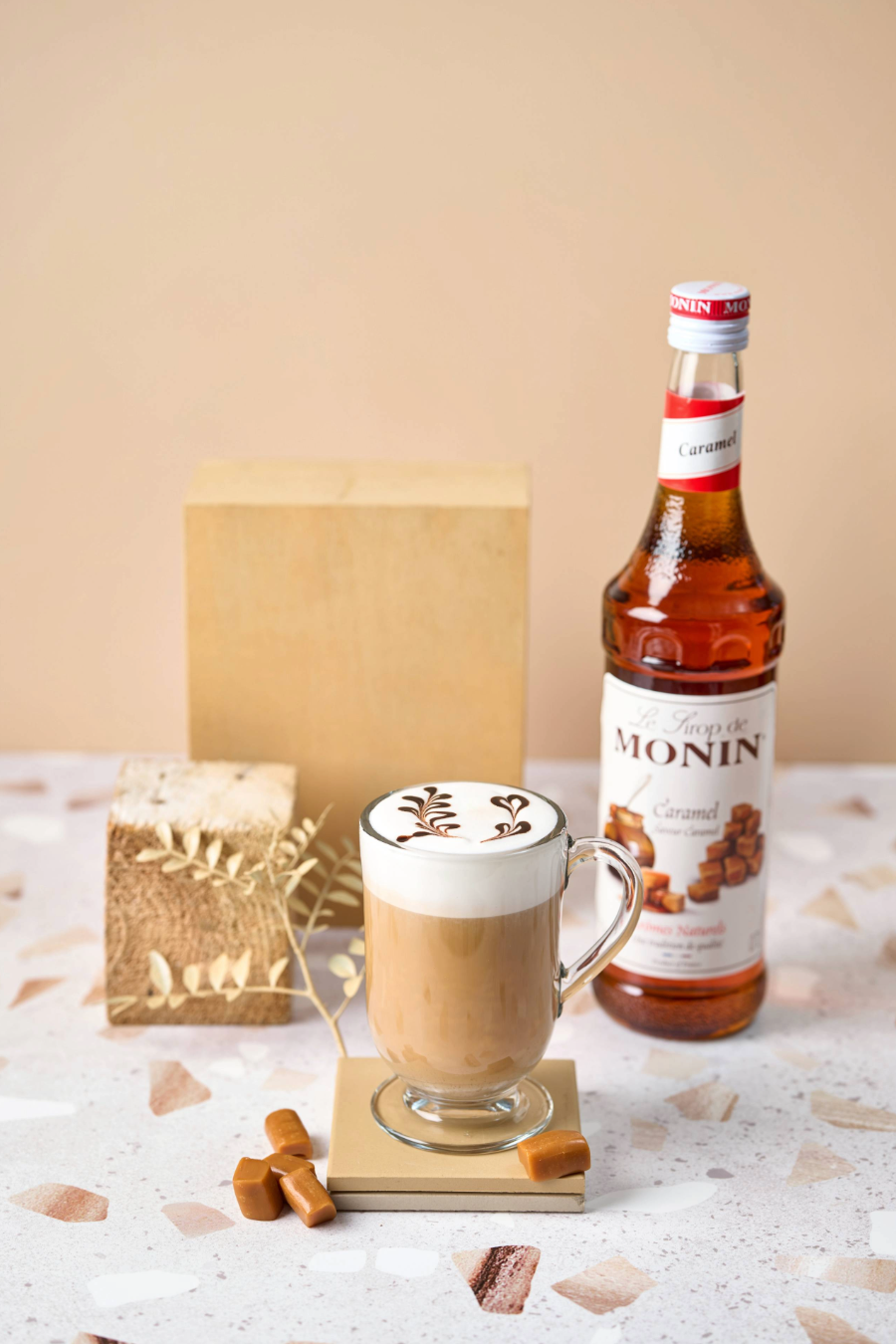 Een glas Monin Caramel latte - grote cappuccino Tevens staat er de fles Monin Caramel 70cl en wat stukjes caramel snoep. Monin verkrijgbaar bij  Sherlocks Place Rotterdam