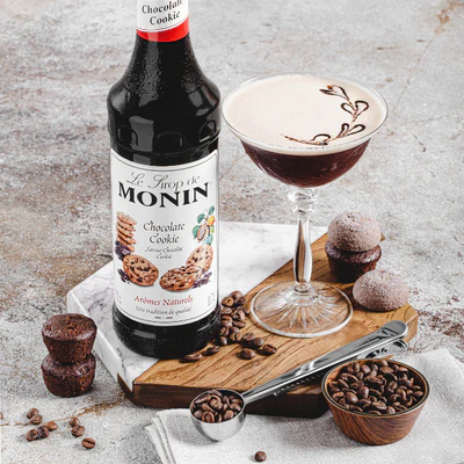 Stijlvolle presentatie van Monin Chocolate Cookie siroop naast een romige chocoladecocktail, omringd door koffiebonen, koekjes en een houten serveerplank – perfect voor barista's en cocktailcreaties.