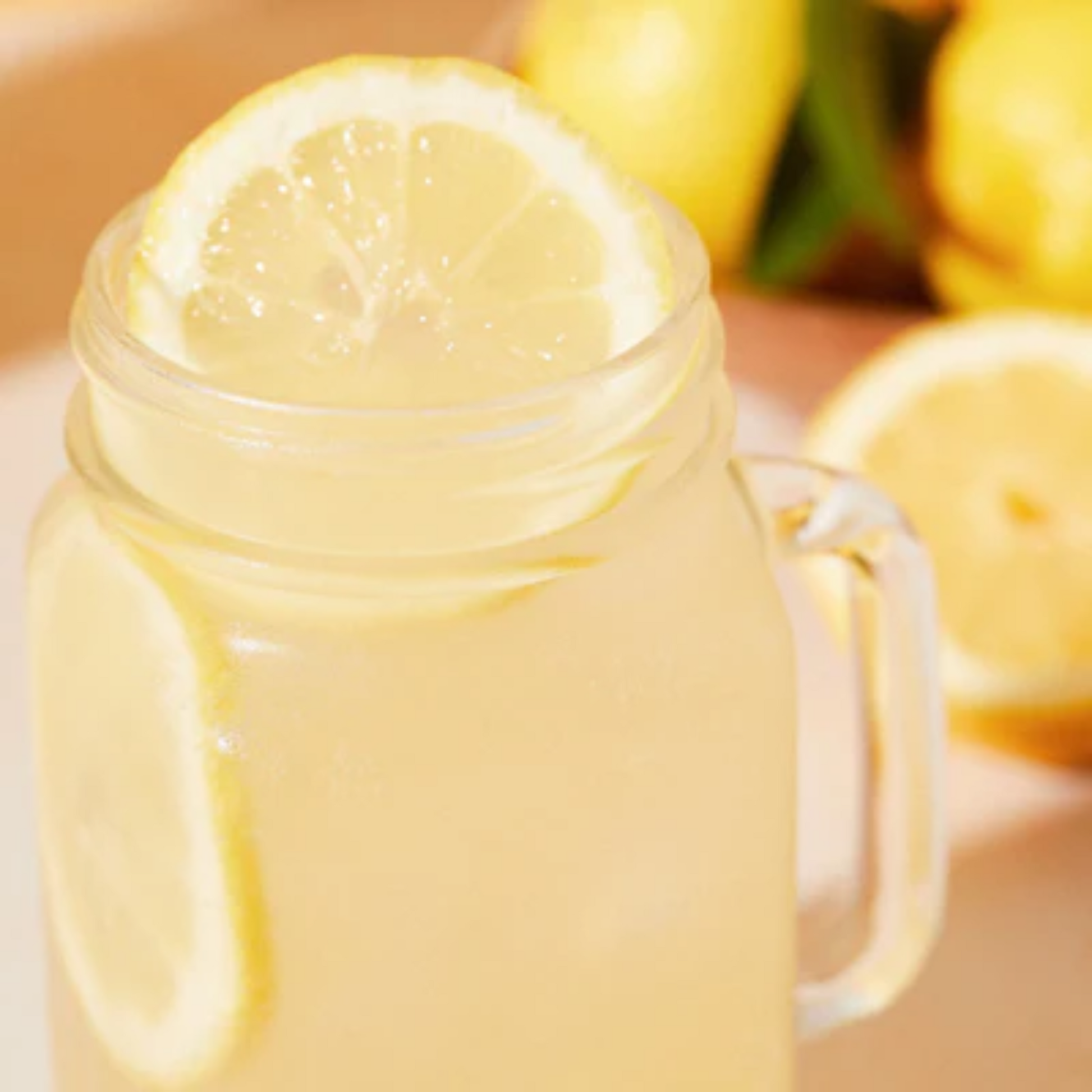 Een close-up foto van een Monin Jar met een homemade Lemonade. De Lemonade is gemaakt met Monin Cloudy Lemon Base siroop, een basis die thuishoort in elke keuken. Deze Lemonade is verrijkt met Yuzu Le Fruit puree. Alles verkrijgbaar bij Sherlocks Place Rotterdam. De Lemonade is gegarneerd met schijfjes citroen en op de achtergrond zie je vaag een paar citroenen.