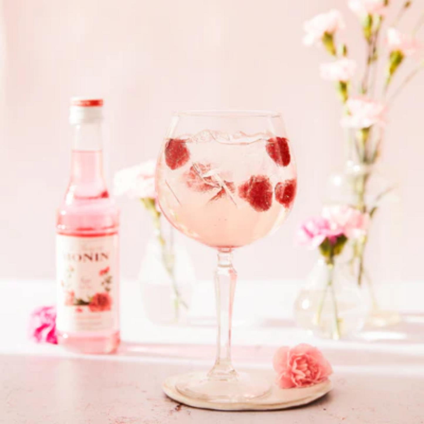 Verfrissende roze soda met frambozen geserveerd in een glas, met Monin Rose siroop op de achtergrond. Verkrijgbaar bij Sherlock's Place in Rotterdam.