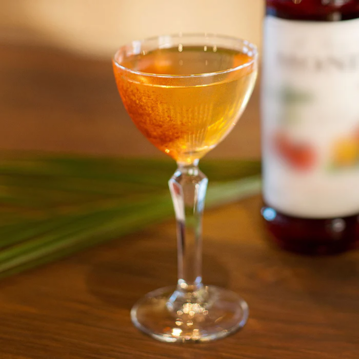 Een glaasje alcoholvrije Tangerine Daiquiri gemaakt met onder meer Monin siroop Caribbean Rum alcoholvrij. Monin verkrijgbaar bij Sherlocks Place Rotterdam. Glas staat p een houten tafel en de kleur van de virgin cocktail is oranje/bruin. Op de achtergrond vaag de fles Monin Mandarijn siroop 70cl